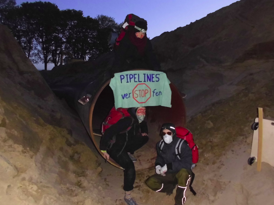Menschen in Pipeline mit Transpi "Pipelines verstopfen"