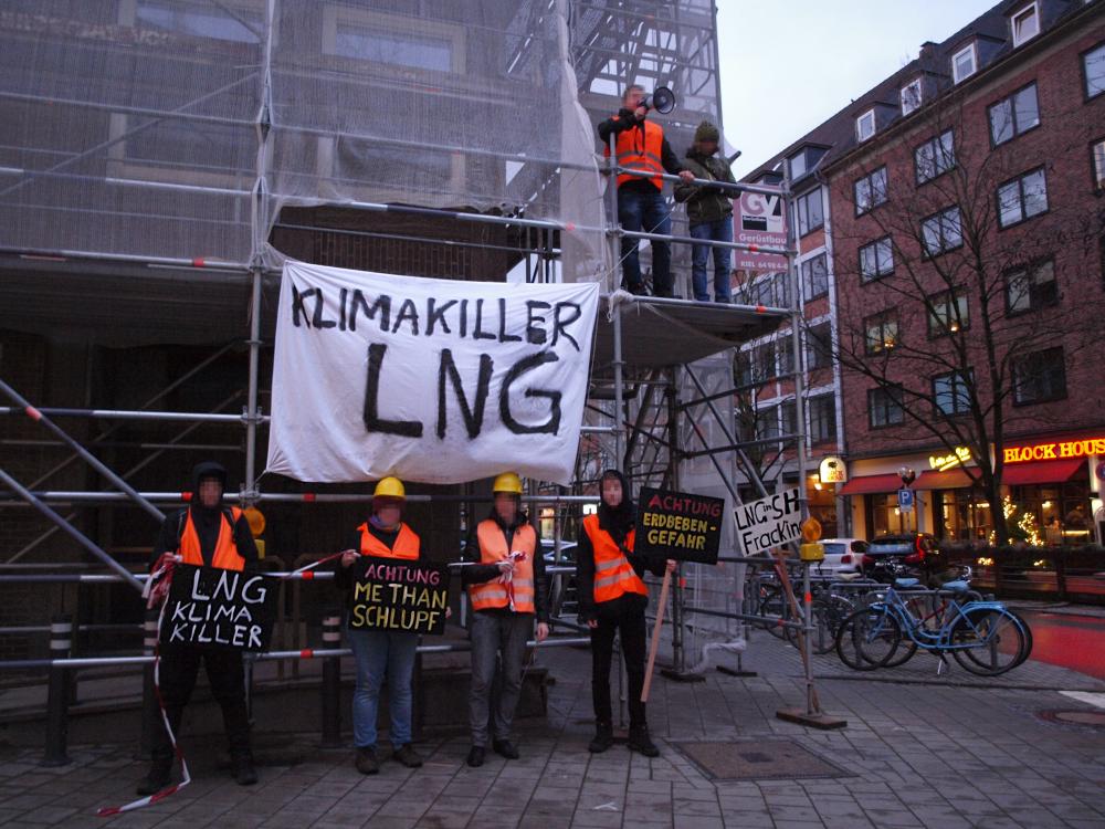 Transparent "Klimakiller LNG" an Baugerüst in Kieler Innenstadt, davor Menschen in Warnwesten mit Baustellenhelmen