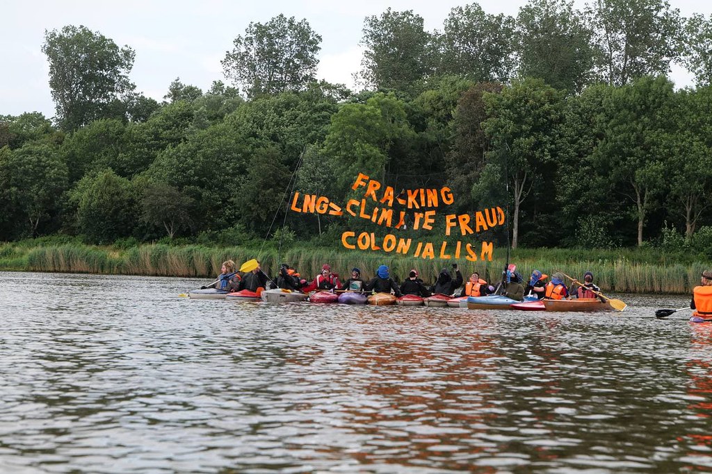 Menschen in Booten auf Nord-Ostsee-Kanal halten Buchstaben hoch: "Fracking LNG = Climate Fraud Colonialism"