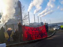Ḿenschen mit Transparent "Vollgas in den Untergang" vor den rauchenden Schornsteinen des Gaskraftwerks in Kiel